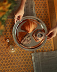 A beautifully set table featuring the Block-Printed Yellow Tablecloth, adorned with a geometric pattern that enhances the warm ambiance. A silver tray with an assortment of pastries sits atop, adding a touch of indulgence to the setting.
