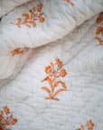 A close-up of the Golden Enigma Quilt, showcasing its intricate hand-block printed floral motifs in a warm golden hue. The soft, handwoven cotton fabric is gently quilted, adding texture and depth to the design. Each delicate stitch reflects the craftsmanship behind this timeless piece, blending elegance and comfort seamlessly.