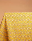 The Block-Printed Yellow Tablecloth drapes elegantly over a table, its intricate geometric pattern radiating warmth and craftsmanship. Framed with a bold yellow border, this piece brings a touch of artisanal charm to any dining space.