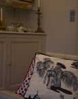 A duo of handcrafted cushions resting on a beige sofa, featuring the Heritage Threads Cushion Cover depicting a black and white Mughal elephant procession, and the Geometric Red Cushion Cover with a bold red and blue pattern. A fusion of heritage craftsmanship and contemporary design, each piece tells a unique story.