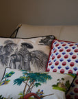 A trio of handcrafted cushions resting on a beige sofa, featuring the Mughal Orchard Cushion Cover with a lush tropical landscape, the Heritage Threads Cushion Cover depicting a black and white Mughal elephant procession, and the Geometric Red Cushion Cover with a bold red and blue pattern. A fusion of heritage craftsmanship and contemporary design, each piece tells a unique story.