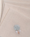 The Veiled Flower Napkin exudes understated elegance with its soft beige cotton weave and delicate embroidery. A single hand-stitched flower in muted blue and white graces the fabric, adding a refined touch to any dining setting. Thoughtfully crafted, its texture and minimalist design celebrate timeless sophistication.