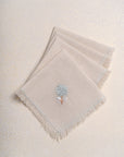 The Veiled Flower Napkin exudes understated elegance with its soft beige cotton weave and delicate embroidery. A single hand-stitched flower in muted blue and white graces the fabric, adding a refined touch to any dining setting. Thoughtfully crafted, its texture and minimalist design celebrate timeless sophistication.