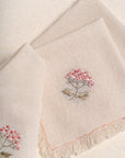 The Misty Garden Napkin brings delicate charm to the dining table with its soft, airy weave and intricate floral embroidery. Hand-stitched blossoms in warm pink tones, complemented by muted green leaves, add a subtle yet elegant touch. Finished with fine fringed edges, this napkin embodies effortless sophistication.