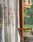 Elegantly Draped Curtains – A delicate, handcrafted curtain made from fine, textured fabric, adorned with intricate hand embroidery and soft pink floral appliqués. Each flower is carefully stitched with subtle detailing, creating a graceful and refined design. The flowing branches and leaves add a natural, organic touch, making these curtains a timeless addition to any elegant home setting.