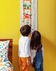 Climber Height Chart – A beautifully handcrafted cotton height chart featuring a vibrant illustration of a wooden plant shelf adorned with lush greenery, colorful pots, and playful garden elements like a straw hat, dragonfly, and butterfly. Hand-stitched details add texture and charm, making it a delightful keepsake for tracking growth milestones.