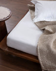 The Ethereal Silk Throw, a luxurious handwoven creation made from the finest mulberry silk. Its soft, rippled texture and delicate tassels exude refinement, draping effortlessly over a bed for a serene, elegant touch.