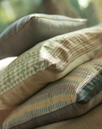 Mehira Silk Cushion Cover, Vivia Cushion Cover, Sofia Cushion Cover – A refined stack of handwoven silk and cotton cushion covers, each showcasing intricate craftsmanship and timeless design. The Mehira Silk Cushion Cover features a luminous weave with geometric accents, the Vivia Cushion Cover presents a soft herringbone-inspired pattern in earthy tones, and the Sofia Cushion Cover blends traditional motifs with delicate stripes. Perfectly layered, these cushions add depth, texture, and elegance to any spa