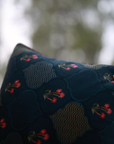 Nargis Cushion Cover – A luxurious fusion of cotton and velvet, this cushion cover features an intricate floral and geometric motif in rich navy blue, highlighted with delicate pink accents. Handcrafted with exceptional detail, its plush texture and vibrant tassel edging add a regal charm to any space.
