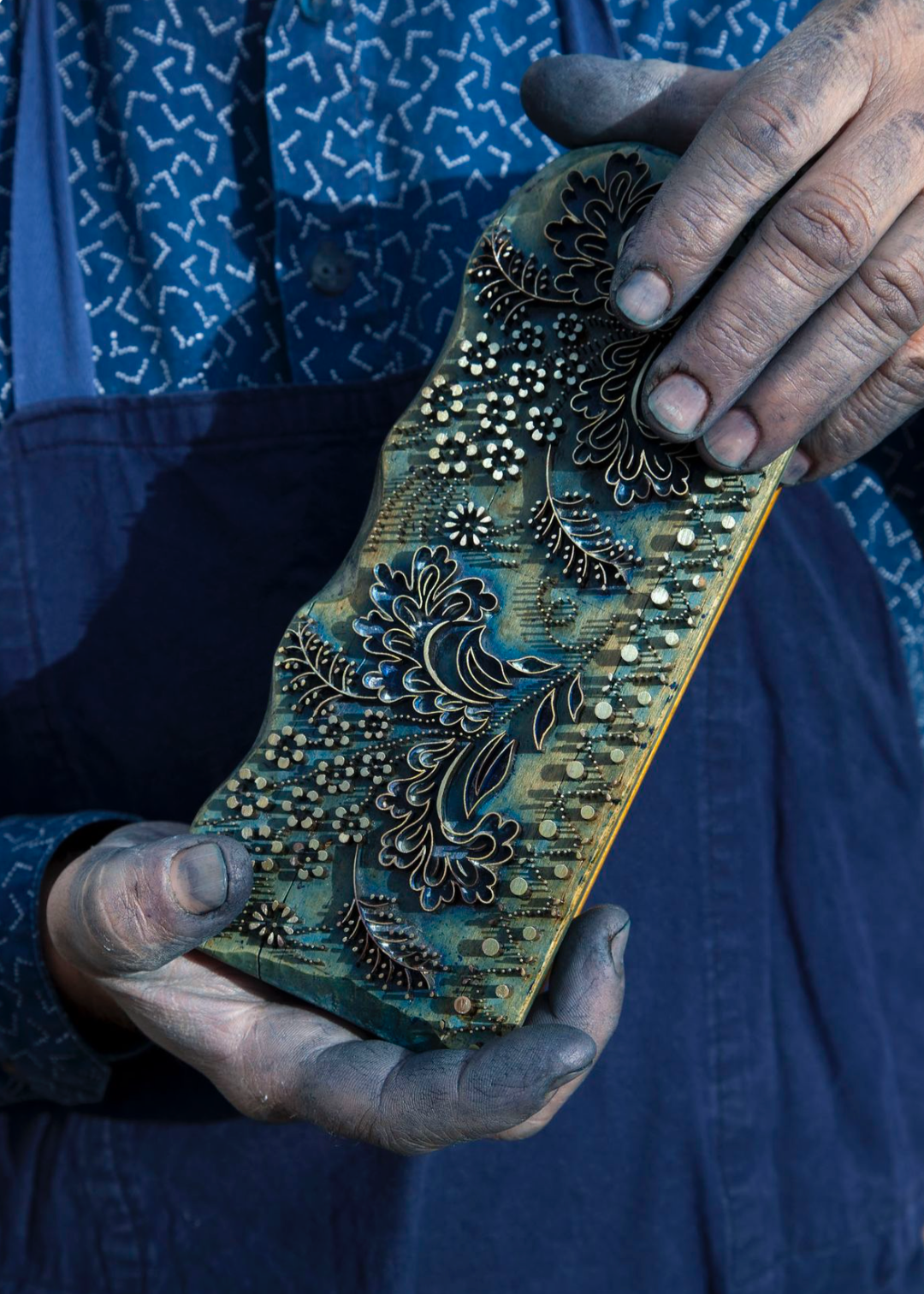 Artisan holding a block used for block printing in India. The color used is Indigo.
