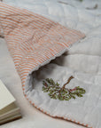 The Trees of Wonder Quilt, crafted from handwoven cotton, features intricate hand-block printed tree motifs that evoke a sense of natural serenity. The soft, quilted texture offers warmth and comfort, while the reversible striped pattern adds versatility to its timeless design. A perfect blend of artistry and coziness for an inviting bedroom.