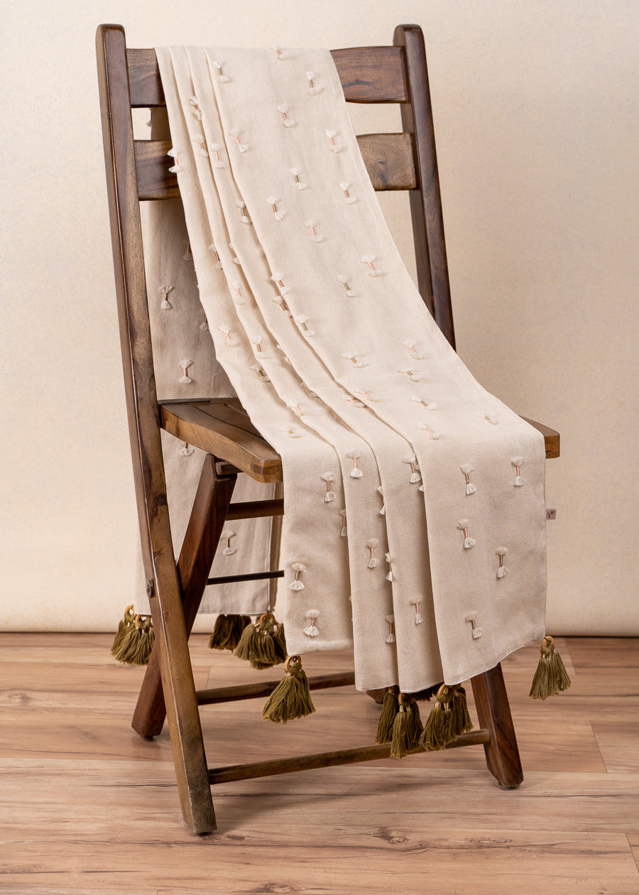 The Bowtie Embrace Throw, a handwoven cotton textile adorned with delicate hand-embroidered bowtie details. Finished with olive-green tassels, this throw brings a soft, textured charm to any space, blending artisanal craftsmanship with understated elegance.