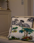 A trio of handcrafted cushions resting on a beige sofa, featuring the Mughal Orchard Cushion Cover with a lush tropical landscape, the Heritage Threads Cushion Cover depicting a black and white Mughal elephant procession, from Idli by Thierry Journo. A fusion of heritage craftsmanship and contemporary design, each piece tells a unique story.