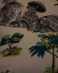 A trio of handcrafted cushions resting on a beige sofa, featuring the Mughal Orchard Cushion Cover with a lush tropical landscape, the Heritage Threads Cushion Cover depicting a black and white Mughal elephant procession, from Idli by Thierry Journo. A fusion of heritage craftsmanship and contemporary design, each piece tells a unique story.