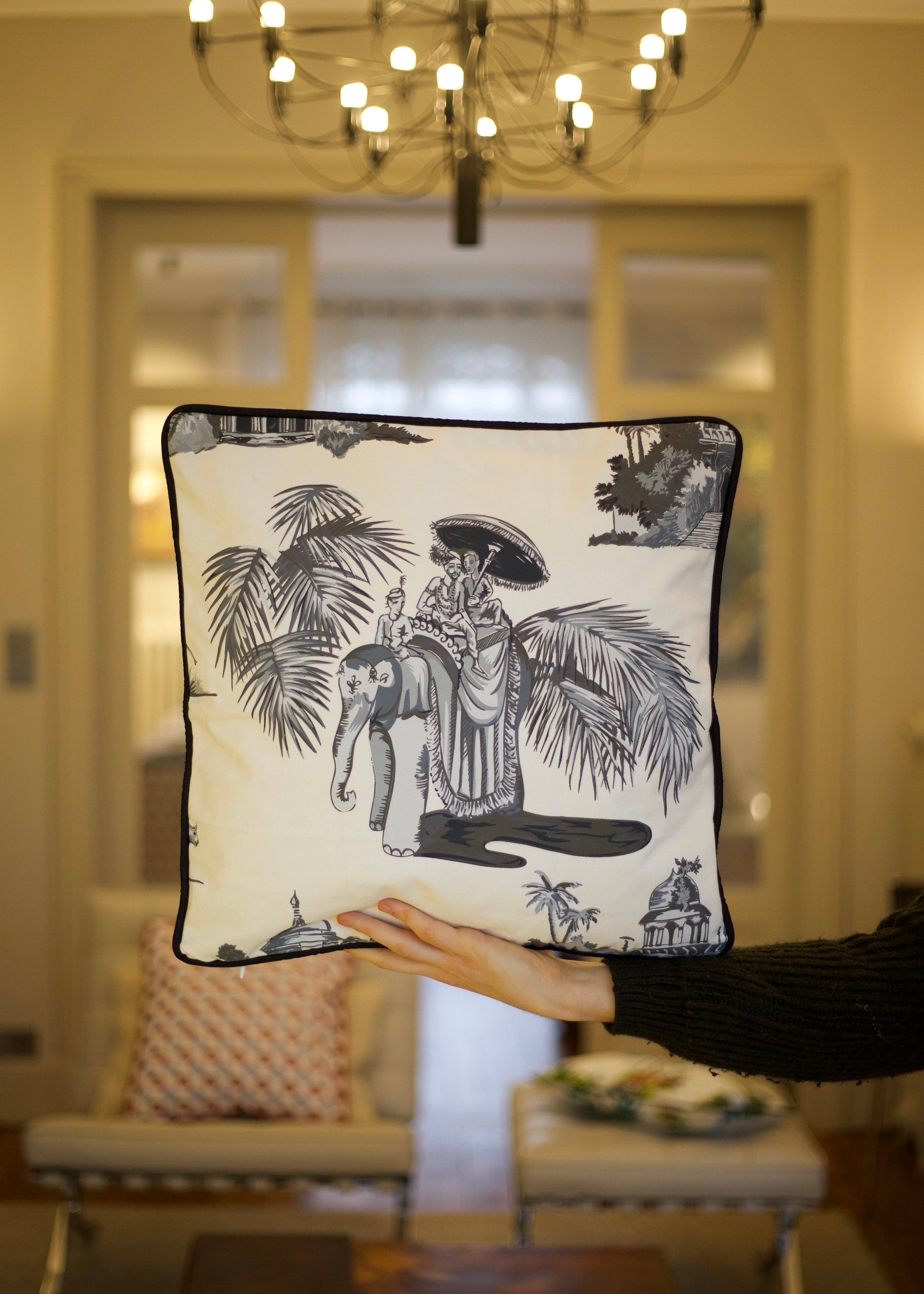 A handcrafted cushion, featuring the Heritage Threads Cushion Cover depicting a black and white Mughal elephant procession, from Idli by Thierry Journo. A fusion of heritage craftsmanship and contemporary design, each piece tells a unique story.