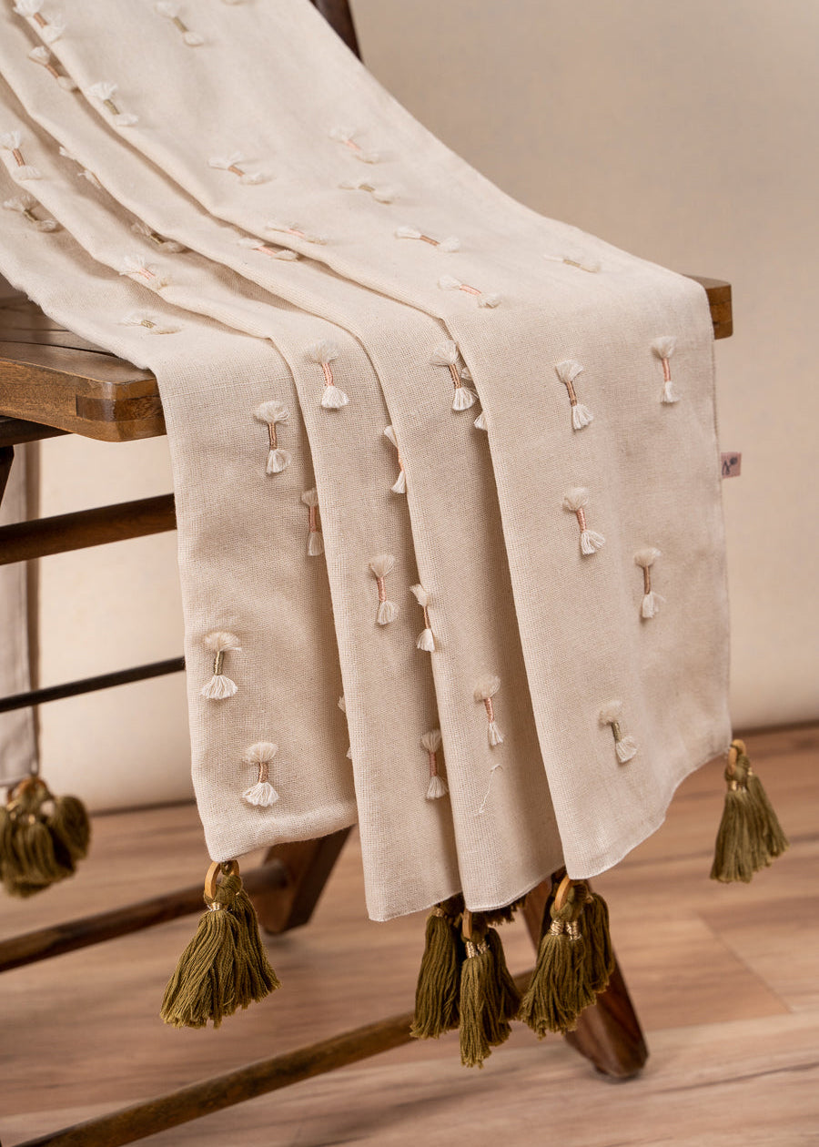 The Bowtie Embrace Throw, a handwoven cotton textile adorned with delicate hand-embroidered bowtie details. Finished with olive-green tassels, this throw brings a soft, textured charm to any space, blending artisanal craftsmanship with understated elegance.