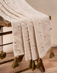 The Bowtie Embrace Throw, a handwoven cotton textile adorned with delicate hand-embroidered bowtie details. Finished with olive-green tassels, this throw brings a soft, textured charm to any space, blending artisanal craftsmanship with understated elegance.