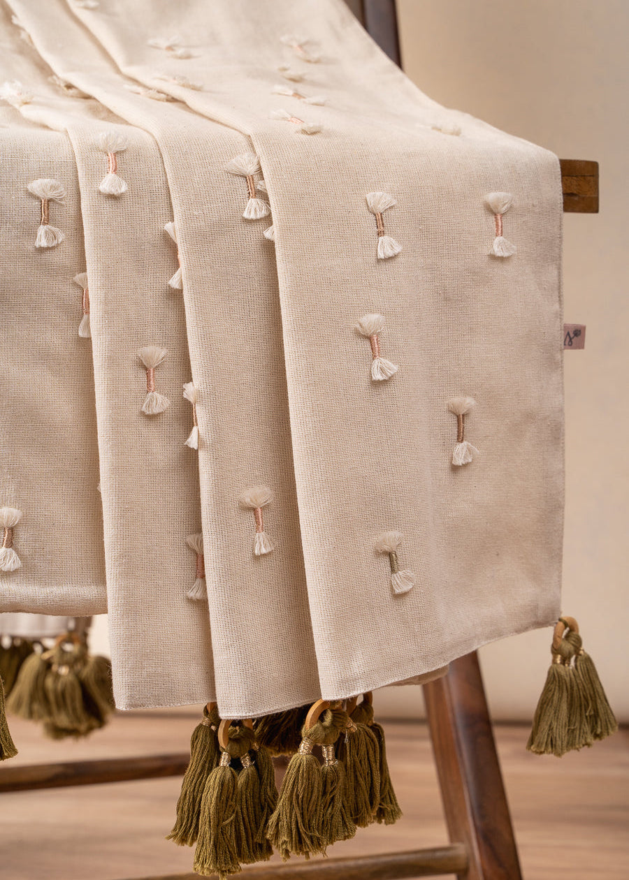 The Bowtie Embrace Throw, a handwoven cotton textile adorned with delicate hand-embroidered bowtie details. Finished with olive-green tassels, this throw brings a soft, textured charm to any space, blending artisanal craftsmanship with understated elegance.