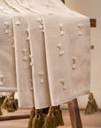 The Bowtie Embrace Throw, a handwoven cotton textile adorned with delicate hand-embroidered bowtie details. Finished with olive-green tassels, this throw brings a soft, textured charm to any space, blending artisanal craftsmanship with understated elegance.