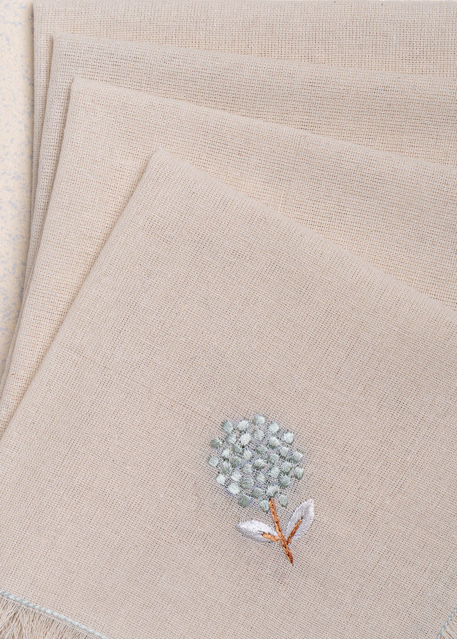The Veiled Flower Napkin exudes understated elegance with its soft beige cotton weave and delicate embroidery. A single hand-stitched flower in muted blue and white graces the fabric, adding a refined touch to any dining setting. Thoughtfully crafted, its texture and minimalist design celebrate timeless sophistication.