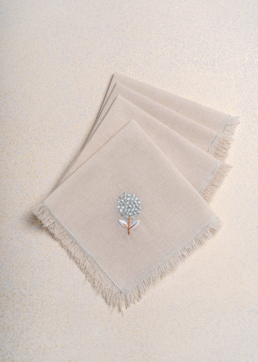 The Veiled Flower Napkin exudes understated elegance with its soft beige cotton weave and delicate embroidery. A single hand-stitched flower in muted blue and white graces the fabric, adding a refined touch to any dining setting. Thoughtfully crafted, its texture and minimalist design celebrate timeless sophistication.