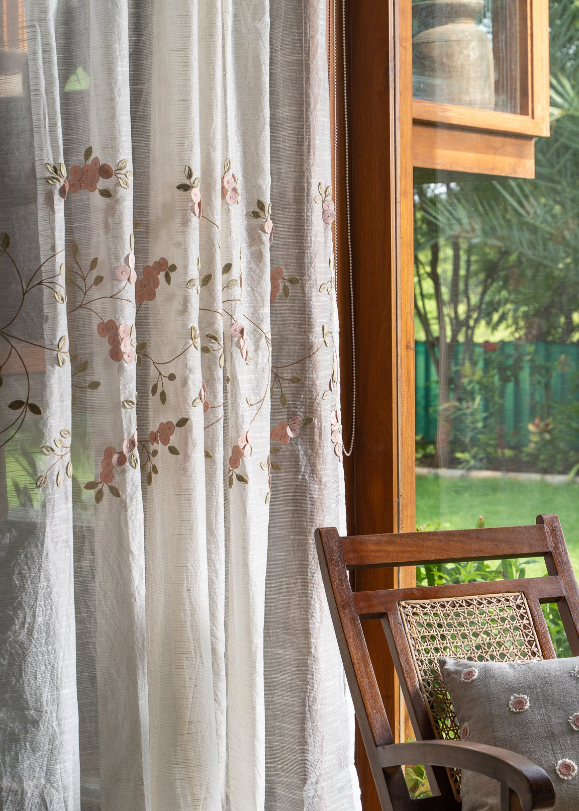 Elegantly Draped Curtains – A delicate, handcrafted curtain made from fine, textured fabric, adorned with intricate hand embroidery and soft pink floral appliqués. Each flower is carefully stitched with subtle detailing, creating a graceful and refined design. The flowing branches and leaves add a natural, organic touch, making these curtains a timeless addition to any elegant home setting.