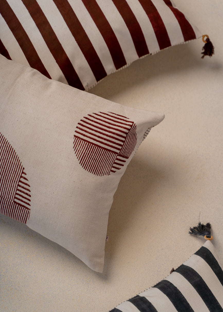 Ember Glow Cushion Cover – A striking cotton cushion cover featuring bold, hand-block-printed stripes in warm earthy tones. Finished with elegant tassels and wooden bead detailing, this artisanal piece adds depth and texture to any space, celebrating traditional craftsmanship with a modern aesthetic.