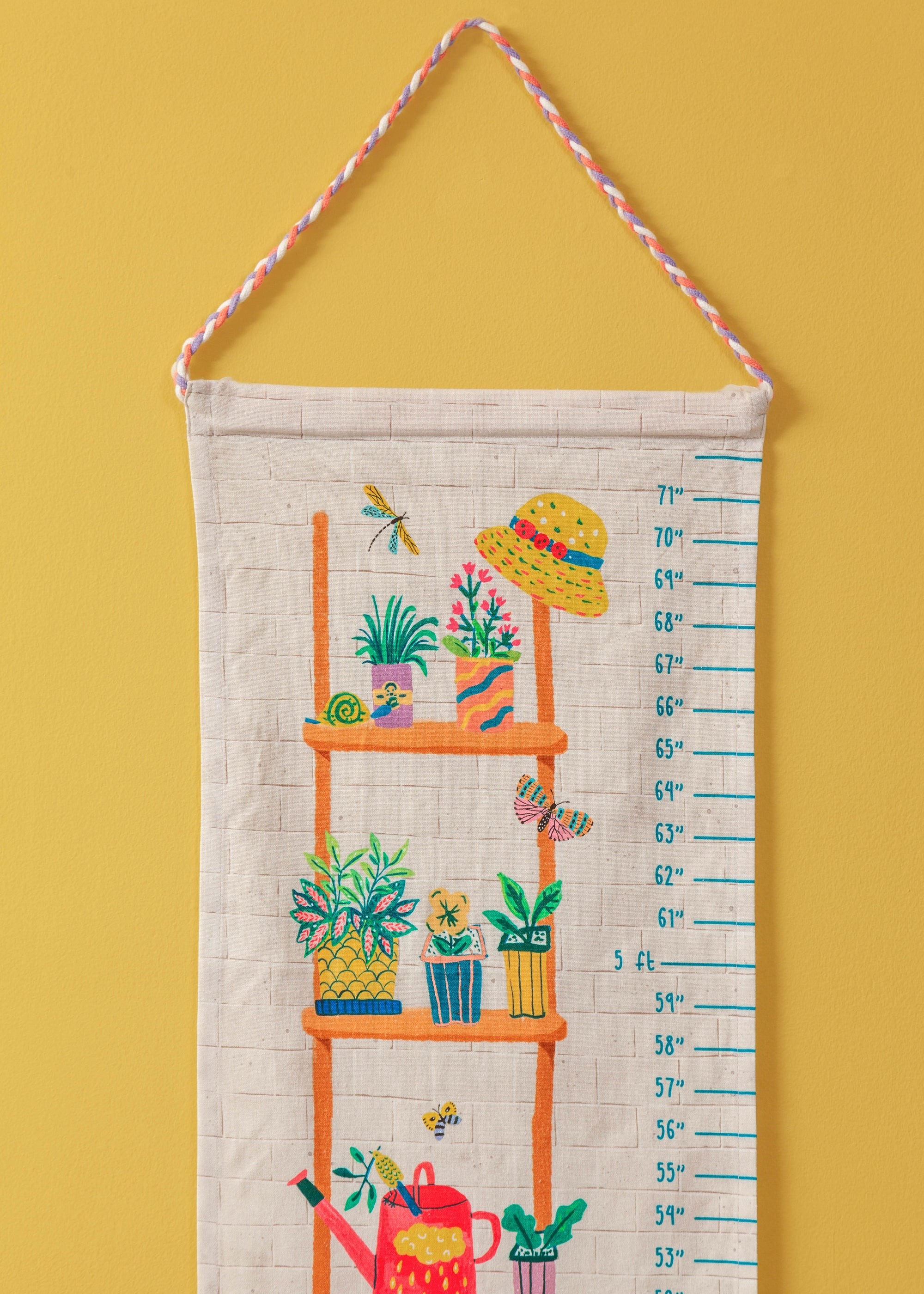 Climber Height Chart – A beautifully handcrafted cotton height chart featuring a vibrant illustration of a wooden plant shelf adorned with lush greenery, colorful pots, and playful garden elements like a straw hat, dragonfly, and butterfly. Hand-stitched details add texture and charm, making it a delightful keepsake for tracking growth milestones.
