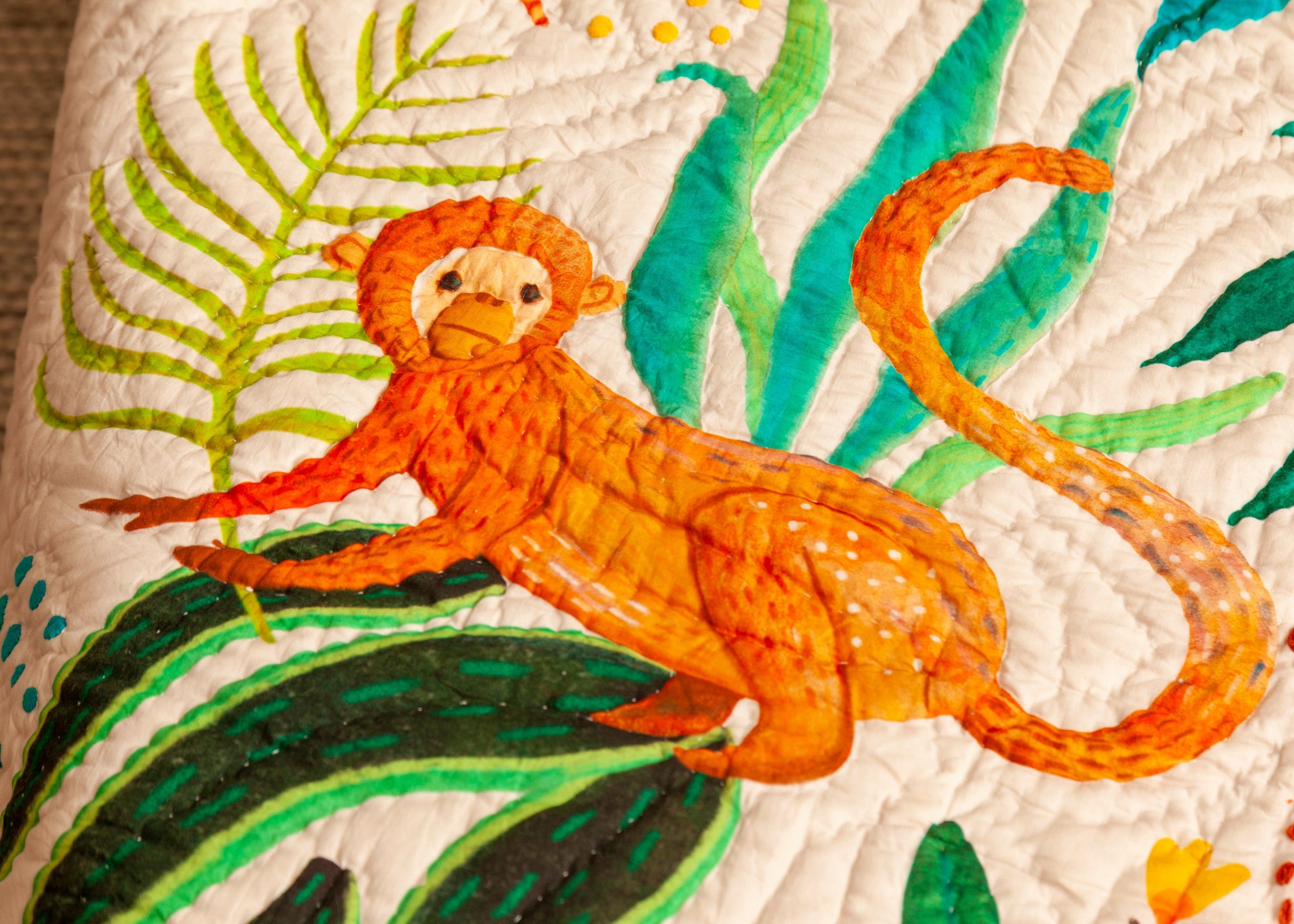A close-up of The Forest is My Playground quilt, handcrafted from cotton, featuring a vibrant illustration of an orange monkey lounging among lush green leaves. The intricate hand-quilting adds texture and depth, highlighting the artisanal craftsmanship. The playful design brings a sense of adventure and warmth to this beautifully made textile piece.