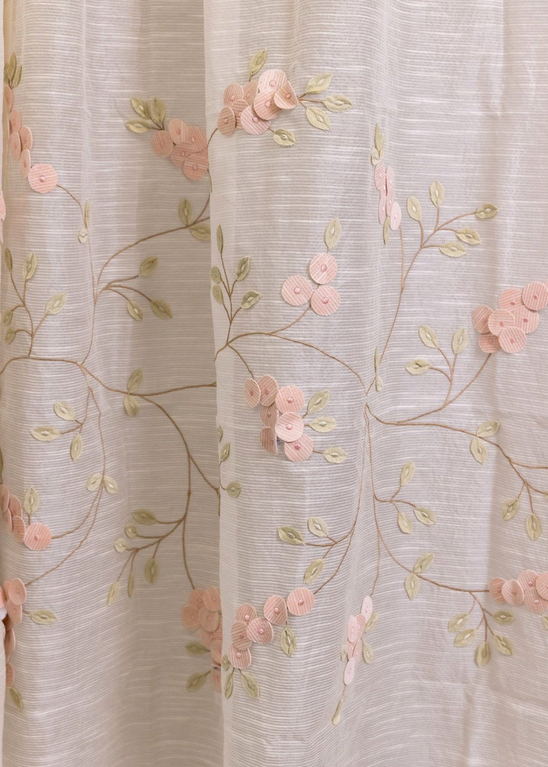 Elegantly Draped Curtains – A delicate, handcrafted curtain made from fine, textured fabric, adorned with intricate hand embroidery and soft pink floral appliqués. Each flower is carefully stitched with subtle detailing, creating a graceful and refined design. The flowing branches and leaves add a natural, organic touch, making these curtains a timeless addition to any elegant home setting.