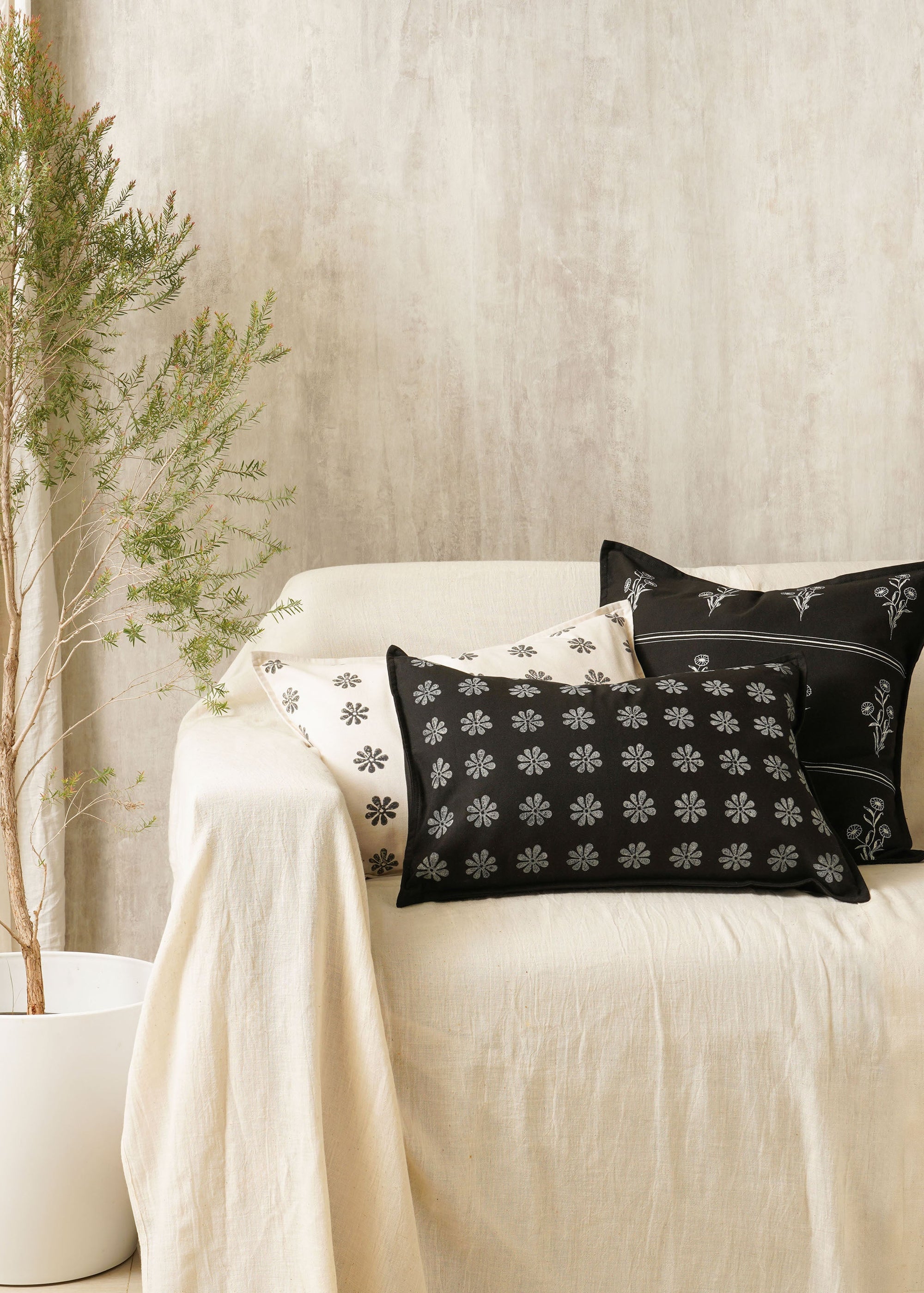 Tara Bloom Cushion Cover – A sophisticated black cushion cover made of cotton, adorned with delicate silver floral motifs, hand-block printed for a timeless appeal. Crafted from high-quality cotton, its refined elegance and monochrome contrast make it a versatile addition to any modern or classic home setting.