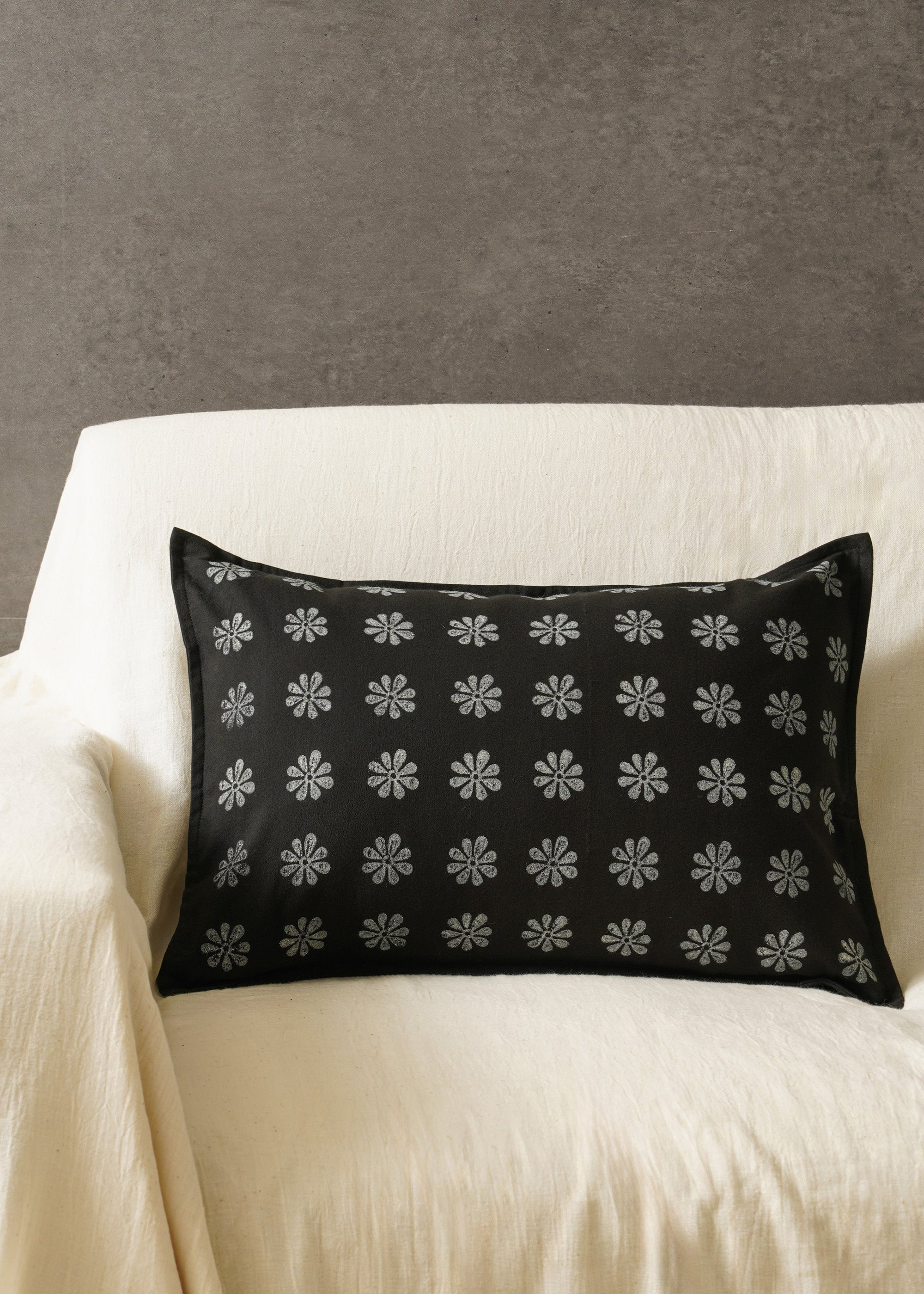 Tara Bloom Cushion Cover – A sophisticated black cushion cover made of cotton, adorned with delicate silver floral motifs, hand-block printed for a timeless appeal. Crafted from high-quality cotton, its refined elegance and monochrome contrast make it a versatile addition to any modern or classic home setting.