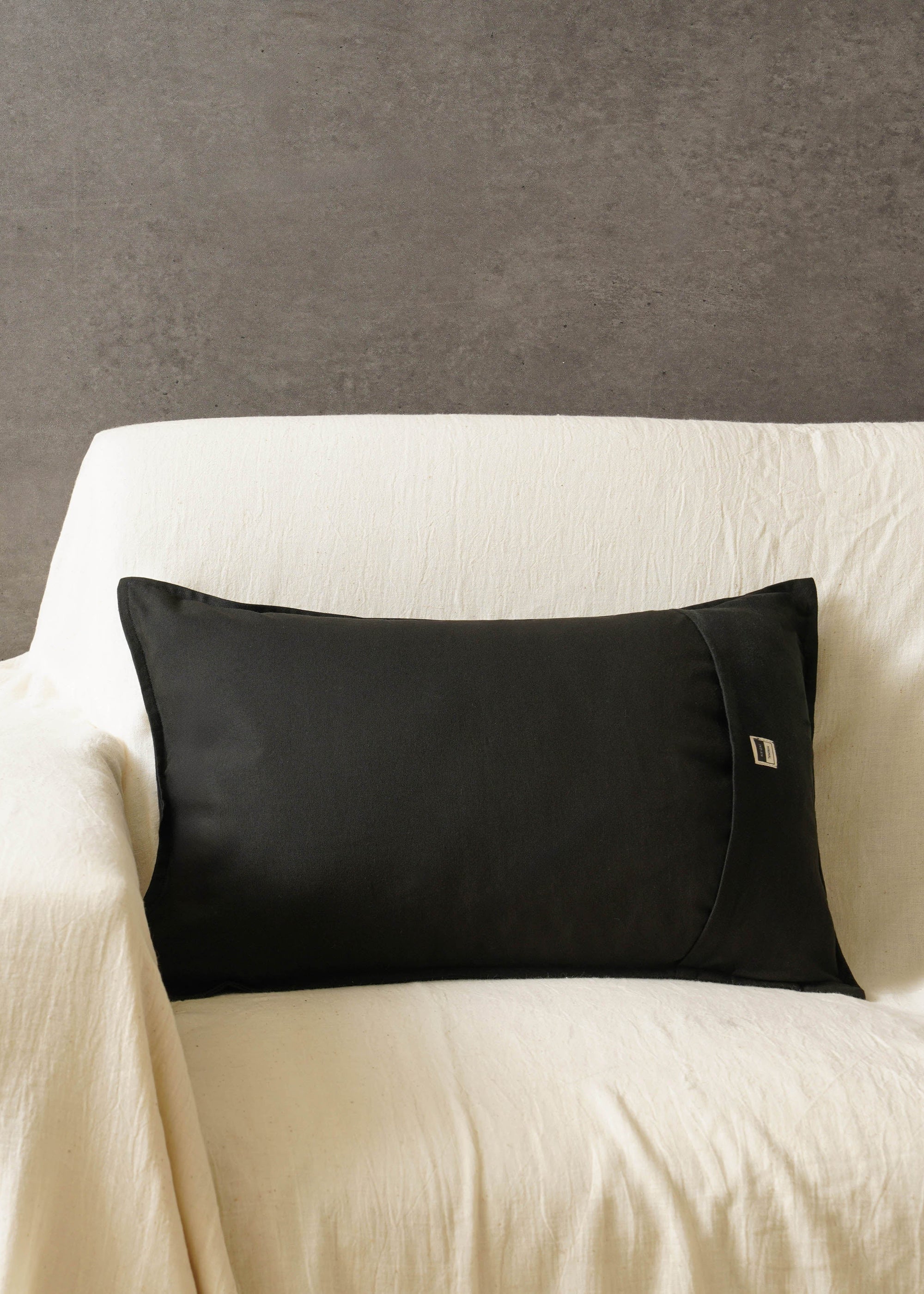 Tara Bloom Cushion Cover – A sophisticated black cushion cover made of cotton, adorned with delicate silver floral motifs, hand-block printed for a timeless appeal. Crafted from high-quality cotton, its refined elegance and monochrome contrast make it a versatile addition to any modern or classic home setting.