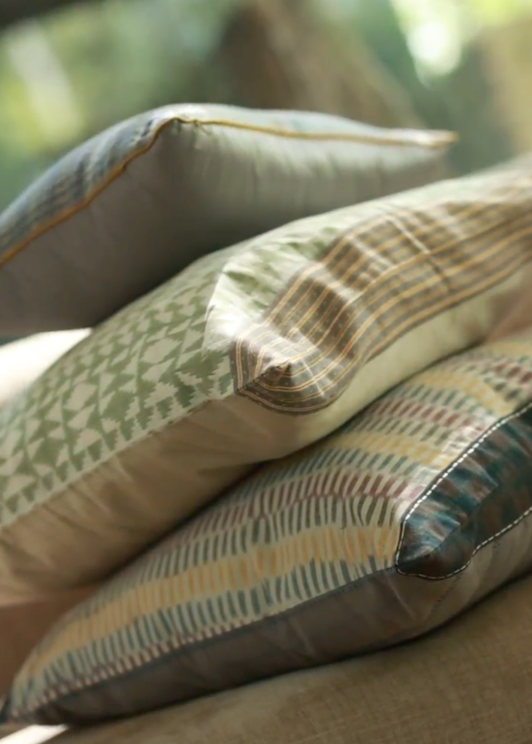 Mehira Silk Cushion Cover, Vivia Cushion Cover, Sofia Cushion Cover – A refined stack of handwoven silk and cotton cushion covers, each showcasing intricate craftsmanship and timeless design. The Mehira Silk Cushion Cover features a luminous weave with geometric accents, the Vivia Cushion Cover presents a soft herringbone-inspired pattern in earthy tones, and the Sofia Cushion Cover blends traditional motifs with delicate stripes. Perfectly layered, these cushions add depth, texture, and elegance to any spa