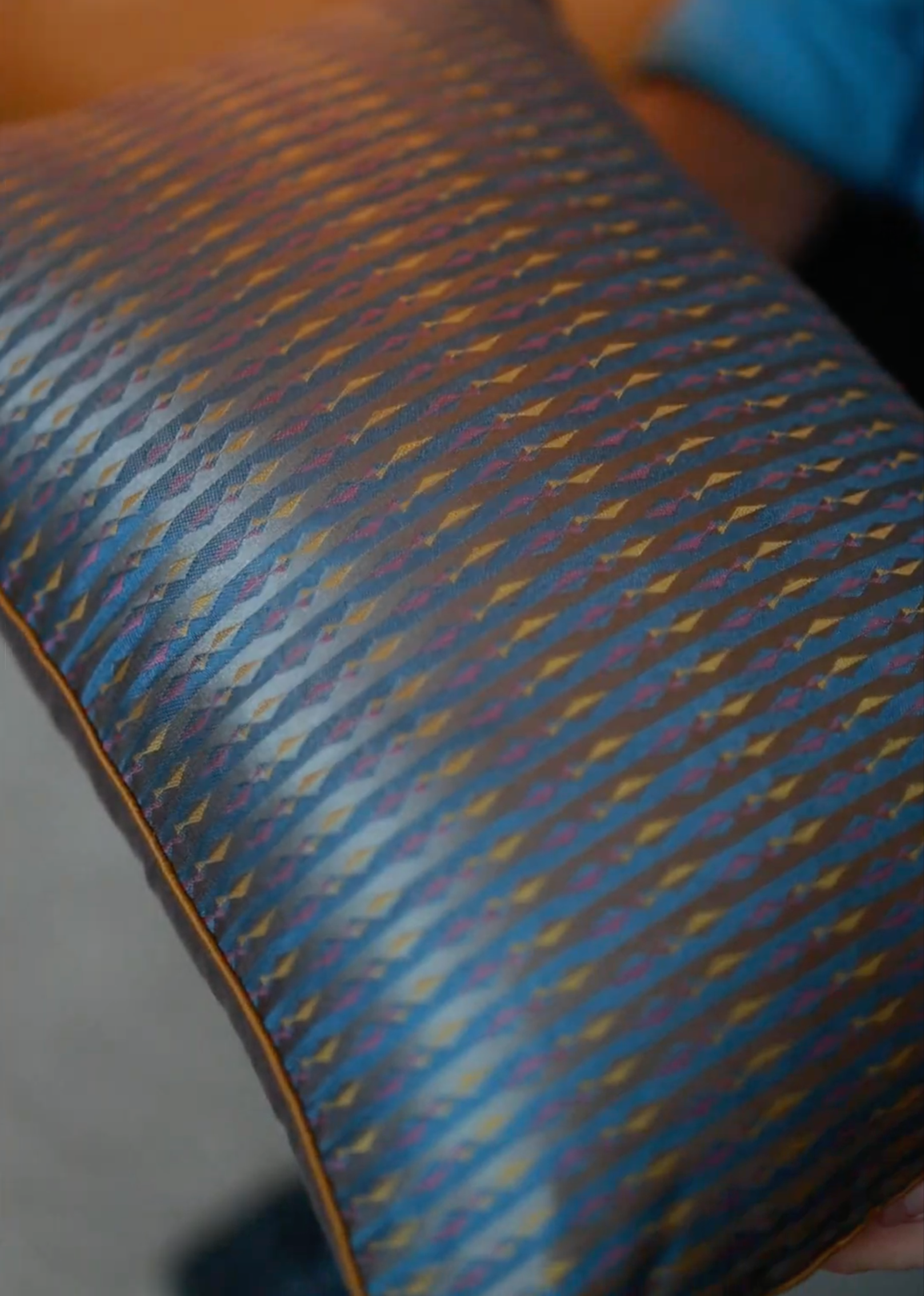 Mehira Silk Cushion Cover – A striking silk cushion cover woven with intricate geometric patterns in deep blue, gold, and maroon hues. The shimmering silk fabric catches the light, revealing a rich interplay of textures and tones. Expertly handcrafted, this cushion cover embodies the finesse of traditional weaving, adding an elegant and sophisticated touch to any space.