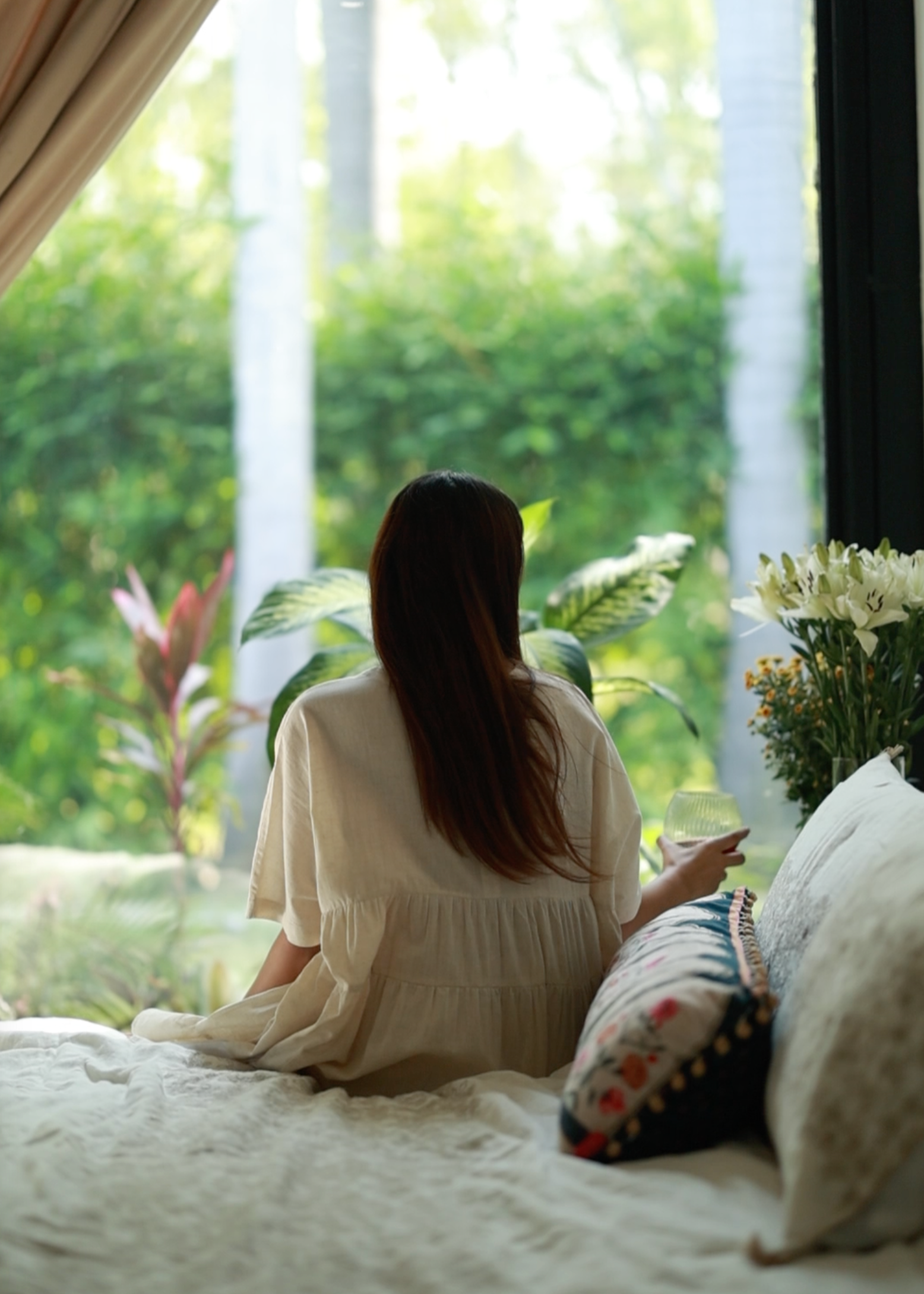 Women looking out the window. Sitting on a handcrafted linen bedspread, with handmade cushion.