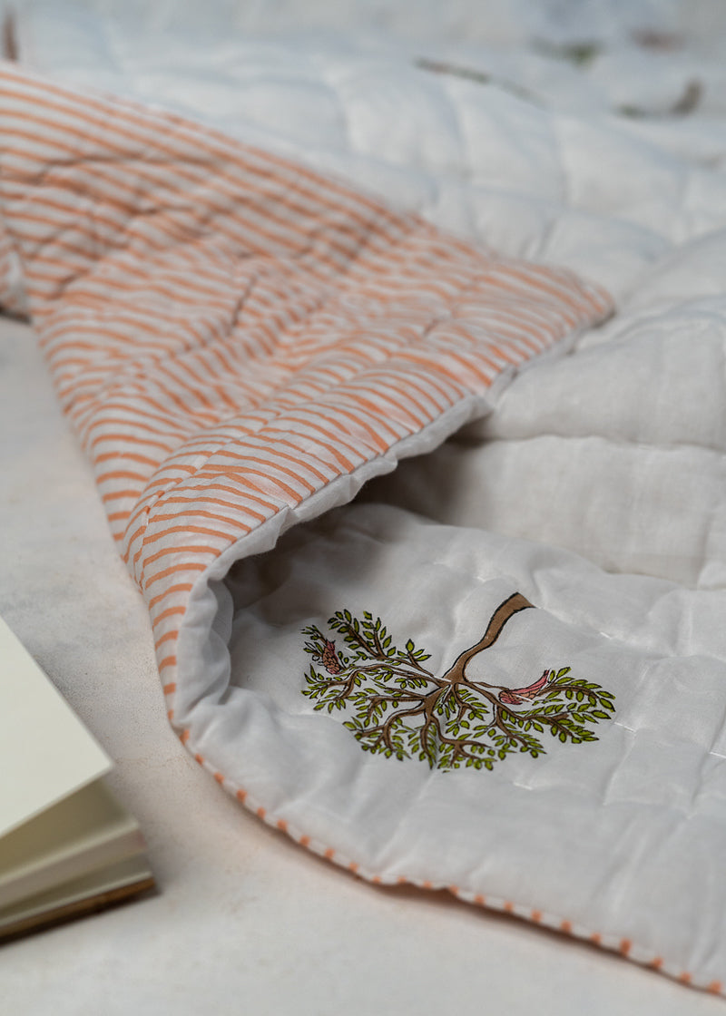 The Trees of Wonder Quilt, crafted from handwoven cotton, features intricate hand-block printed tree motifs that evoke a sense of natural serenity. The soft, quilted texture offers warmth and comfort, while the reversible striped pattern adds versatility to its timeless design. A perfect blend of artistry and coziness for an inviting bedroom.